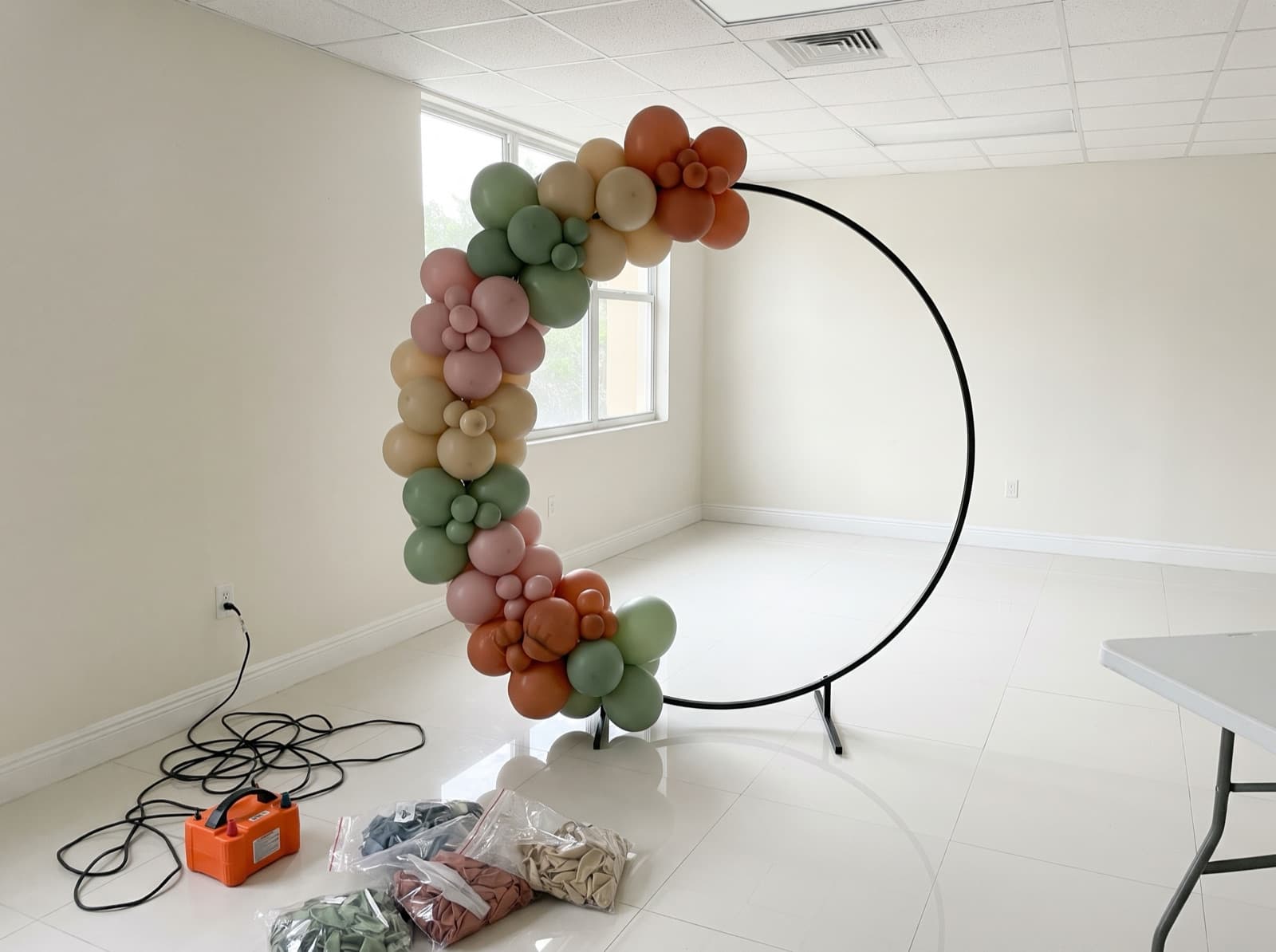 Organic balloon garland in progress on an arch frame in an empty party room