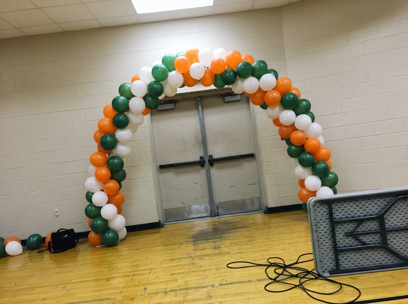 Spiral balloon arch in orange and green over a school gym entrance