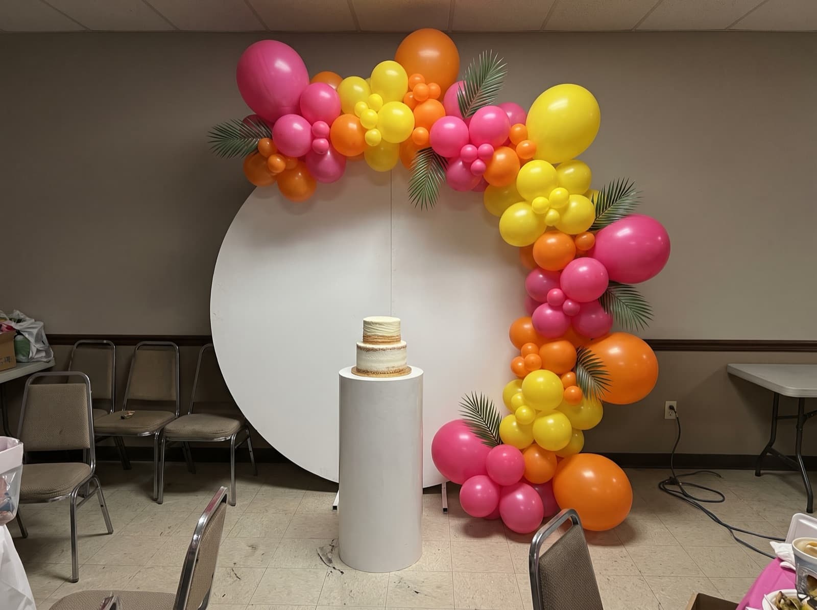 Round balloon backdrop with a tropical garland and a cake pedestal at a Miami birthday party