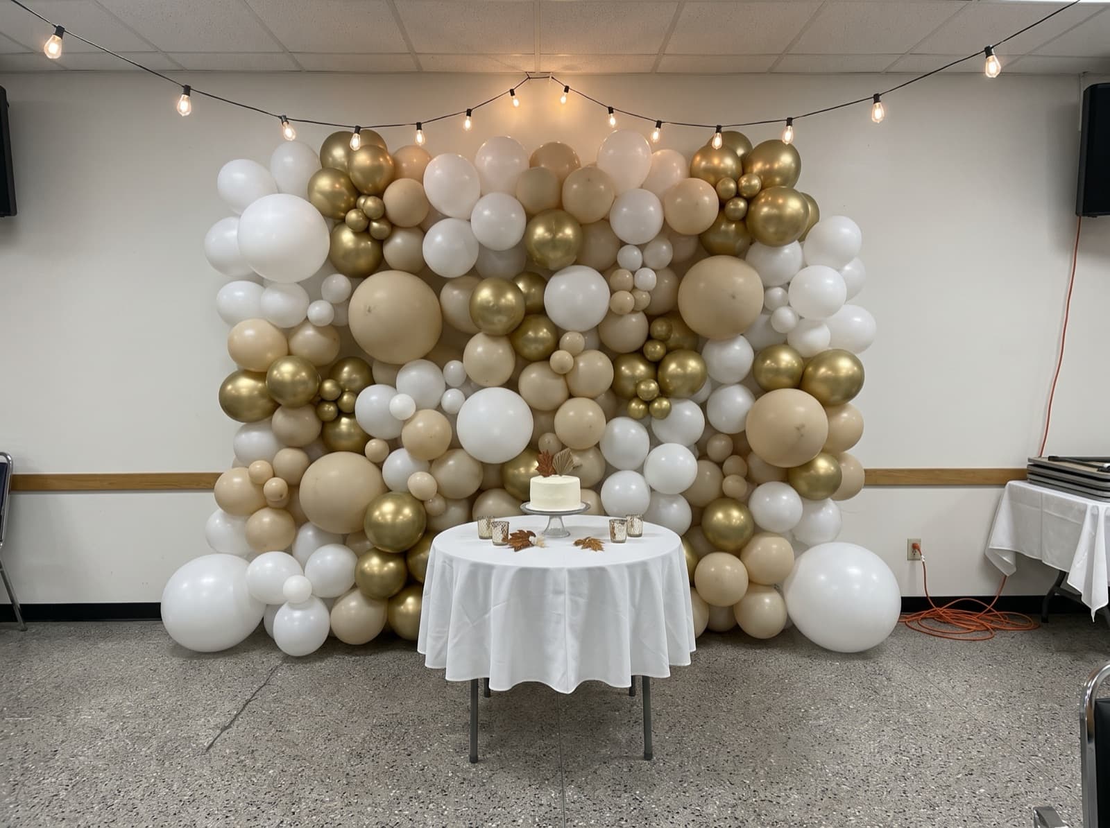 Organic balloon wall in white, sand and gold behind a cake table in a Miami banquet hall